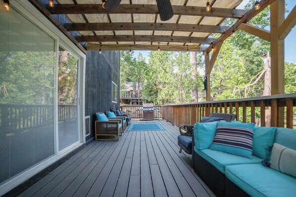 Una terraza techada con mobiliario exterior, una parrilla y vistas a los árboles circundantes.
