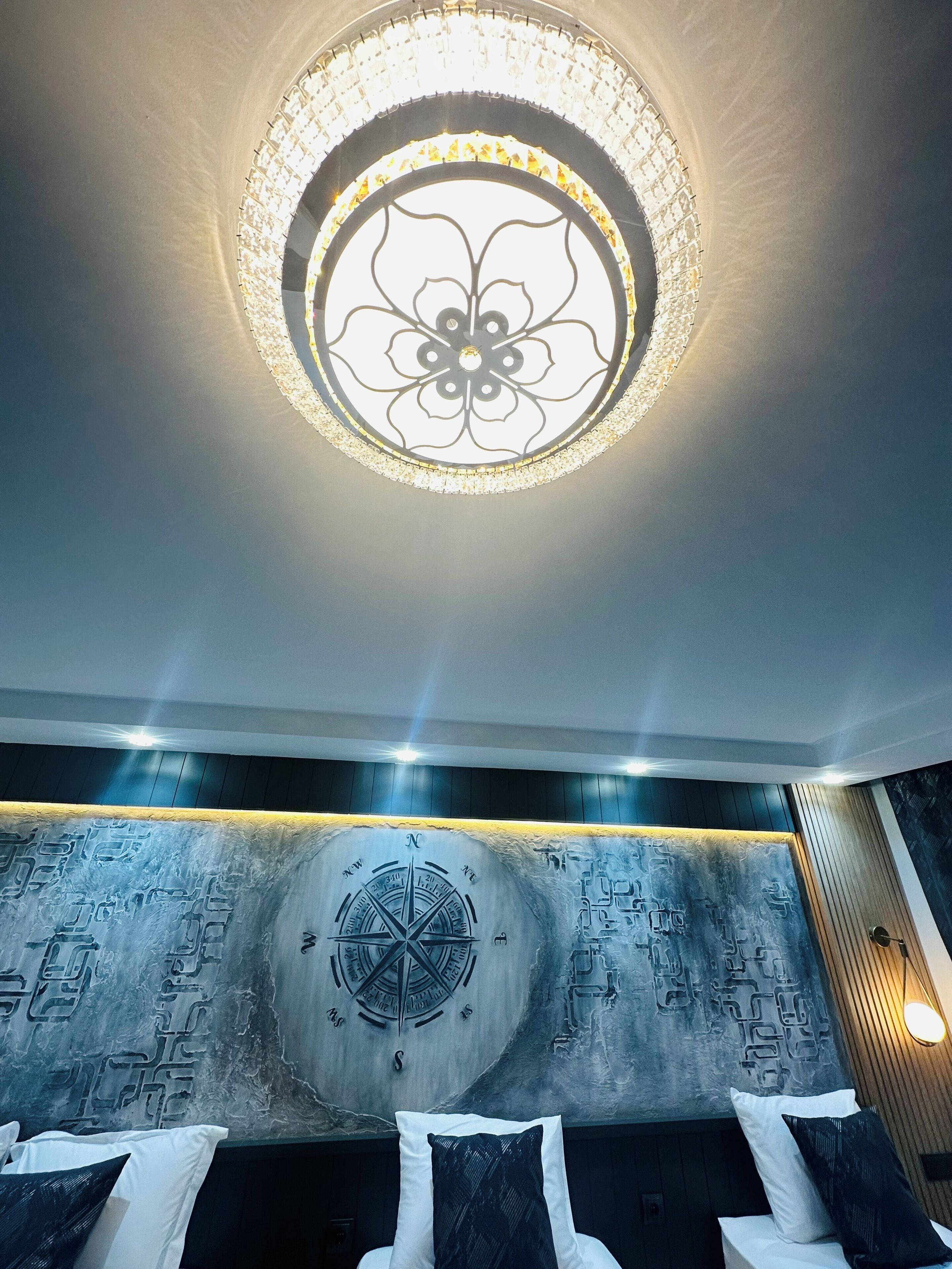 A room with a circular ceiling light fixture, a wall with a compass design, and a bed with pillows.