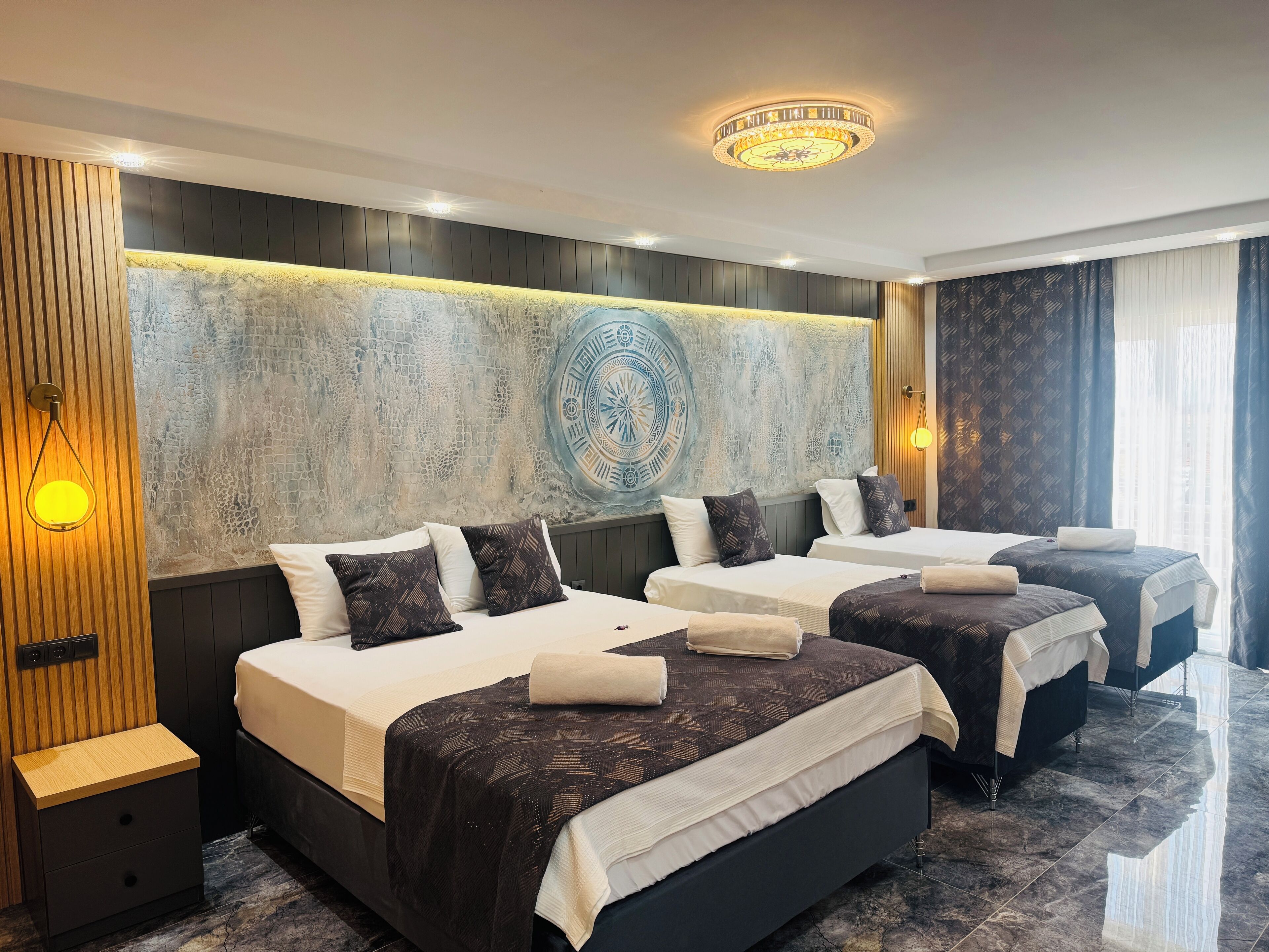 A hotel room with three beds, a large decorative wall, and a modern chandelier.