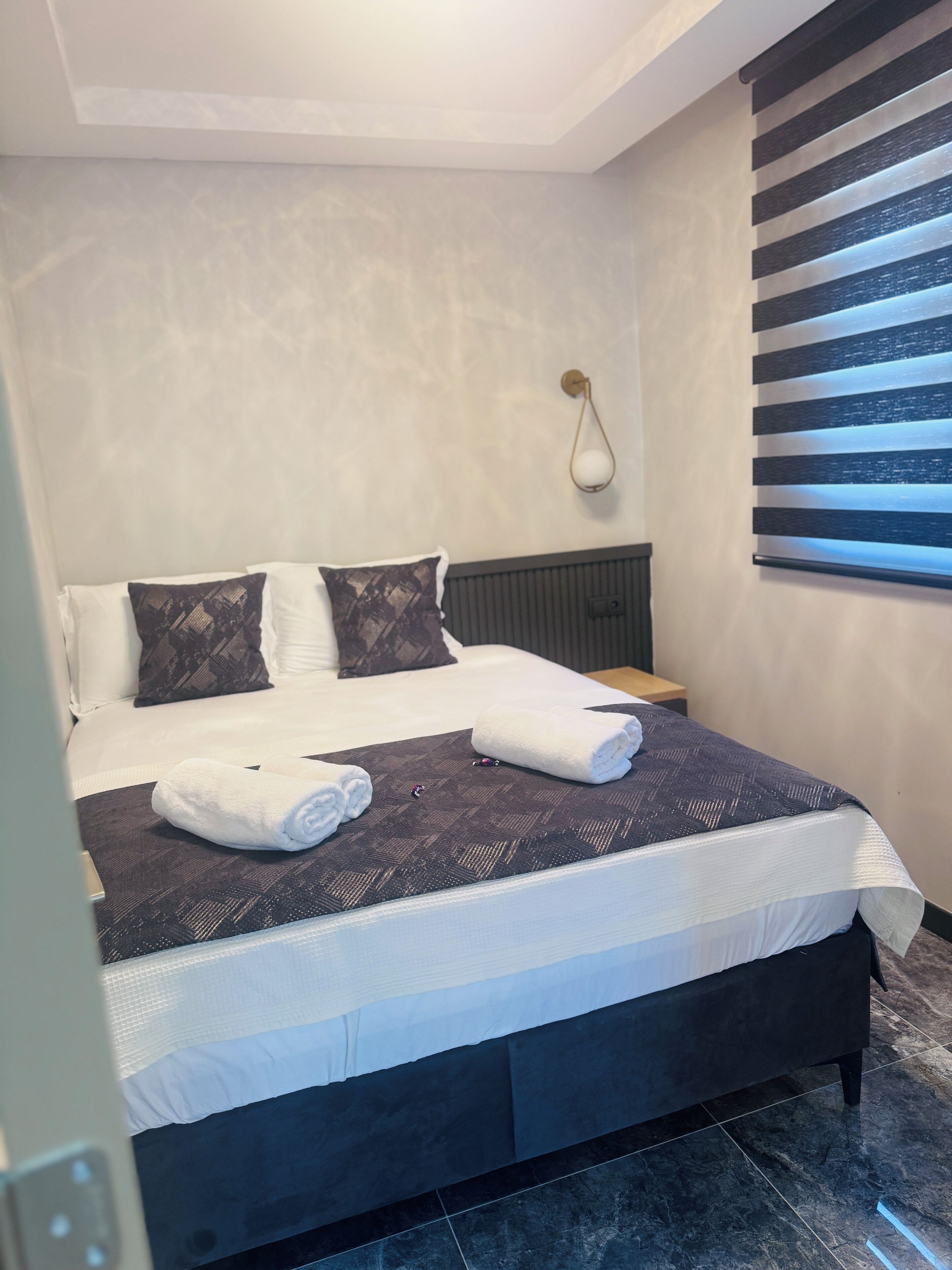 Een net opgemaakt bed met witte lakens, een donker beddekleed en twee sierkussens.