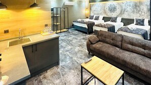Ein modernes Wohnzimmer mit einer Couch, einem kleinen Holztisch und einer Küchenzeile mit Spüle und Pendelleuchten.