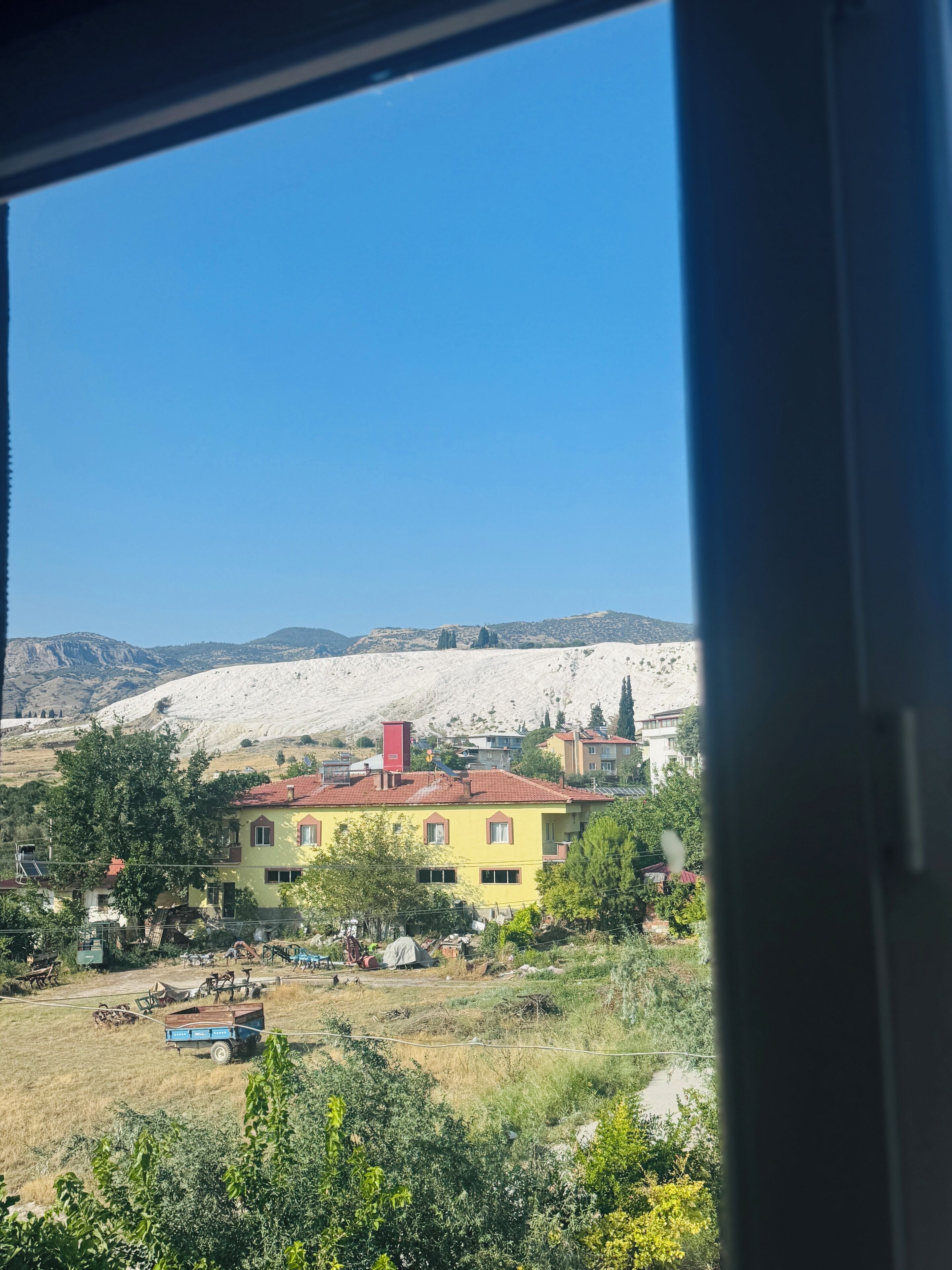 Ein gelbes Gebäude mit rotem Dach, umgeben von Grün und einer Berglandschaft.