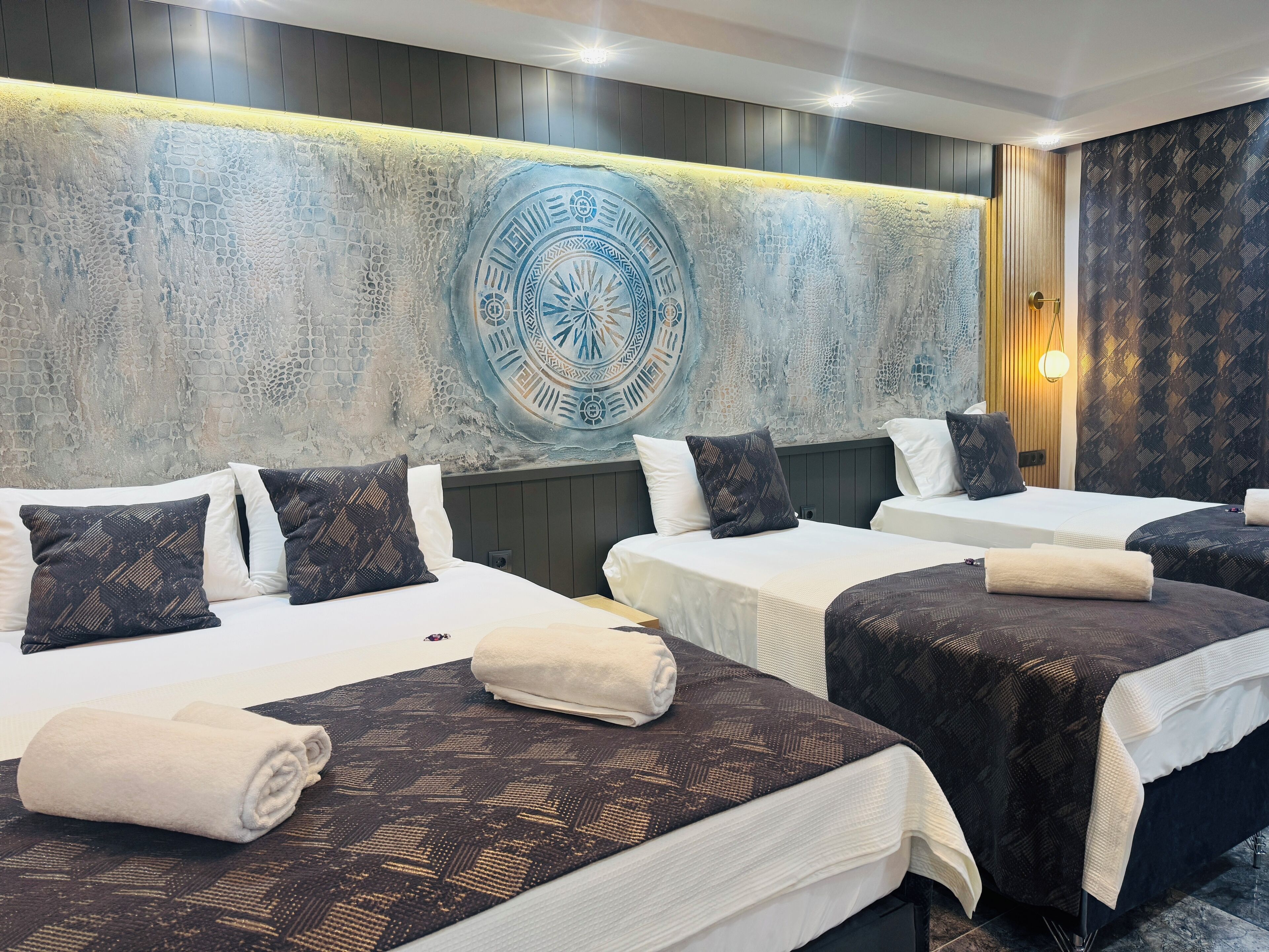 Habitación de hotel con dos camas, cada una con una colcha y almohadas estampadas, un amplio mural decorativo y una lámpara moderna.