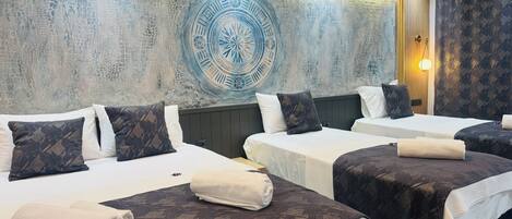 Habitación de hotel con dos camas, cada una con una colcha y almohadas estampadas, un amplio mural decorativo y una lámpara moderna.