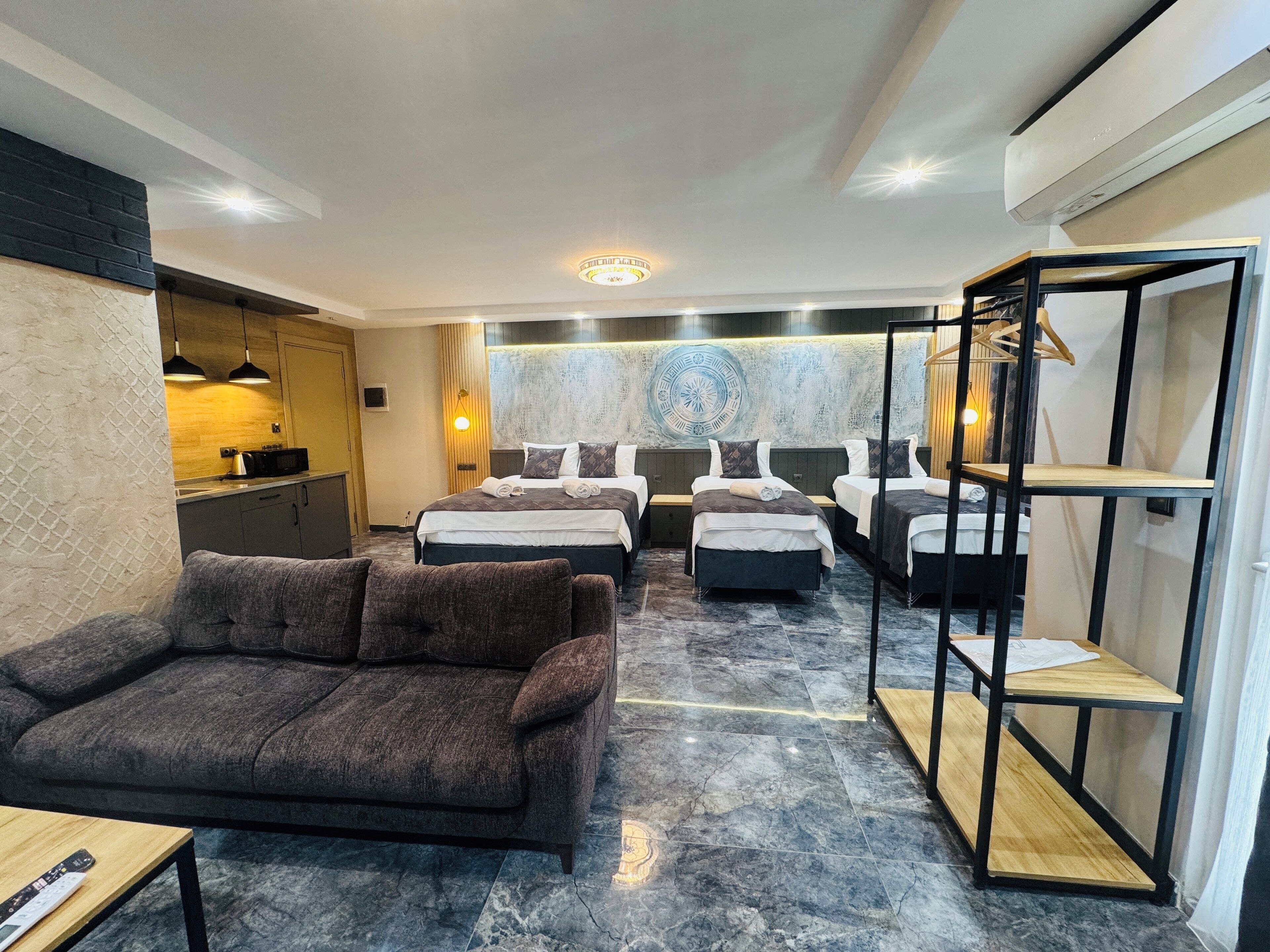 Una habitación de hotel moderna con sofá, tres camas, zona de cocina y una pared decorativa.