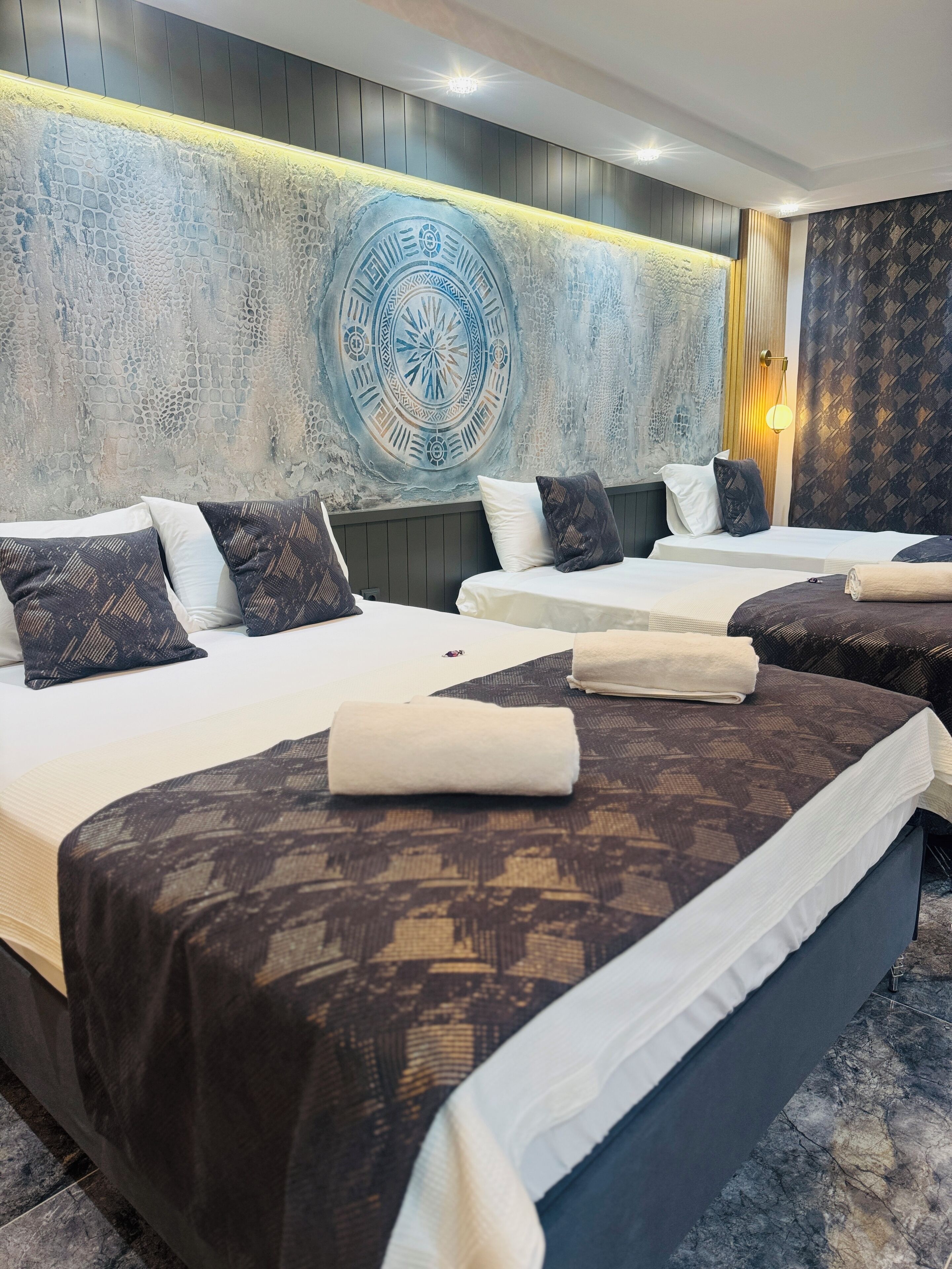 Une chambre d’hôtel avec deux lits, chacun agrémenté de draps et d’oreillers à motifs. Un mur décoratif présente un motif circulaire, et un luminaire est fixé au mur.