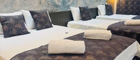 Habitación de hotel con dos camas, cada una con ropa de cama y almohadas estampadas. Se observa una pared decorativa con un diseño circular y una lámpara fijada a la pared.