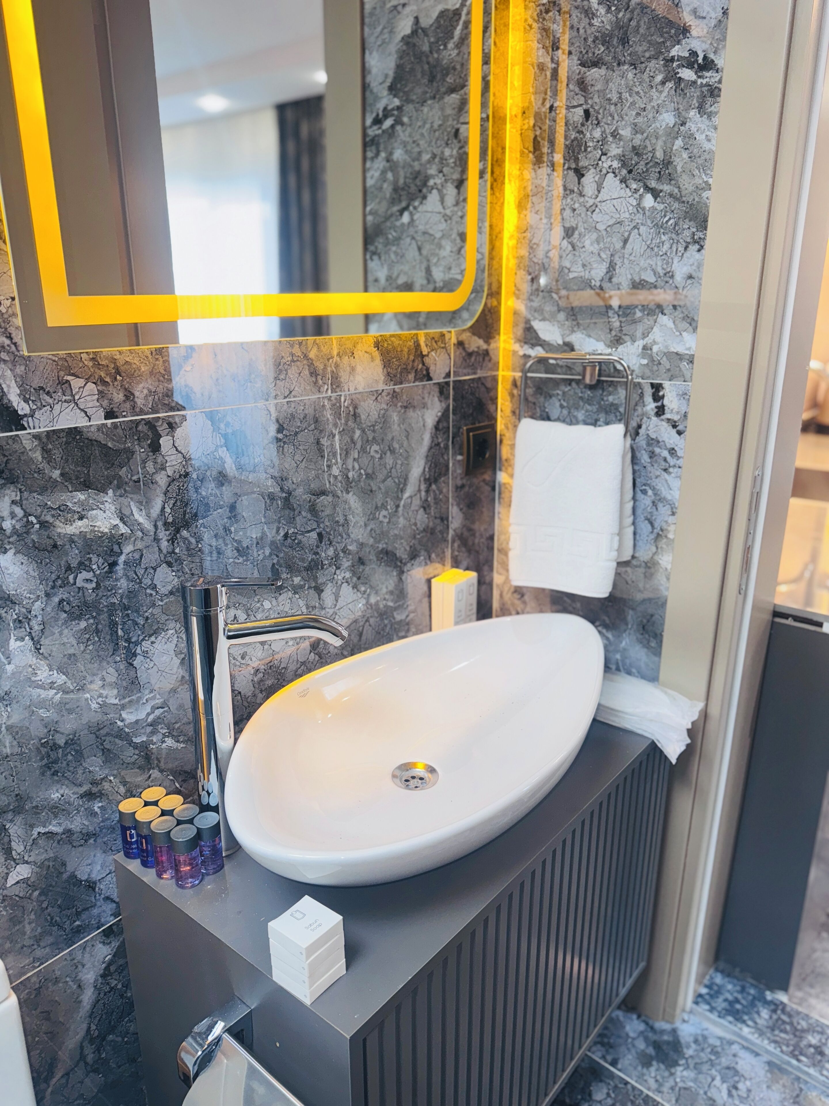 A modern bathroom with a white sink, a mirror with a yellow frame, and a towel rack.