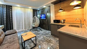 A modern living room with a sofa, a wooden coffee table, and a TV. The room has a kitchen area with a sink and a microwave. - Tikir House (Denizli)