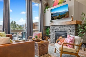 A cozy living room with a fireplace, comfortable seating, and a large window overlooking a scenic view.