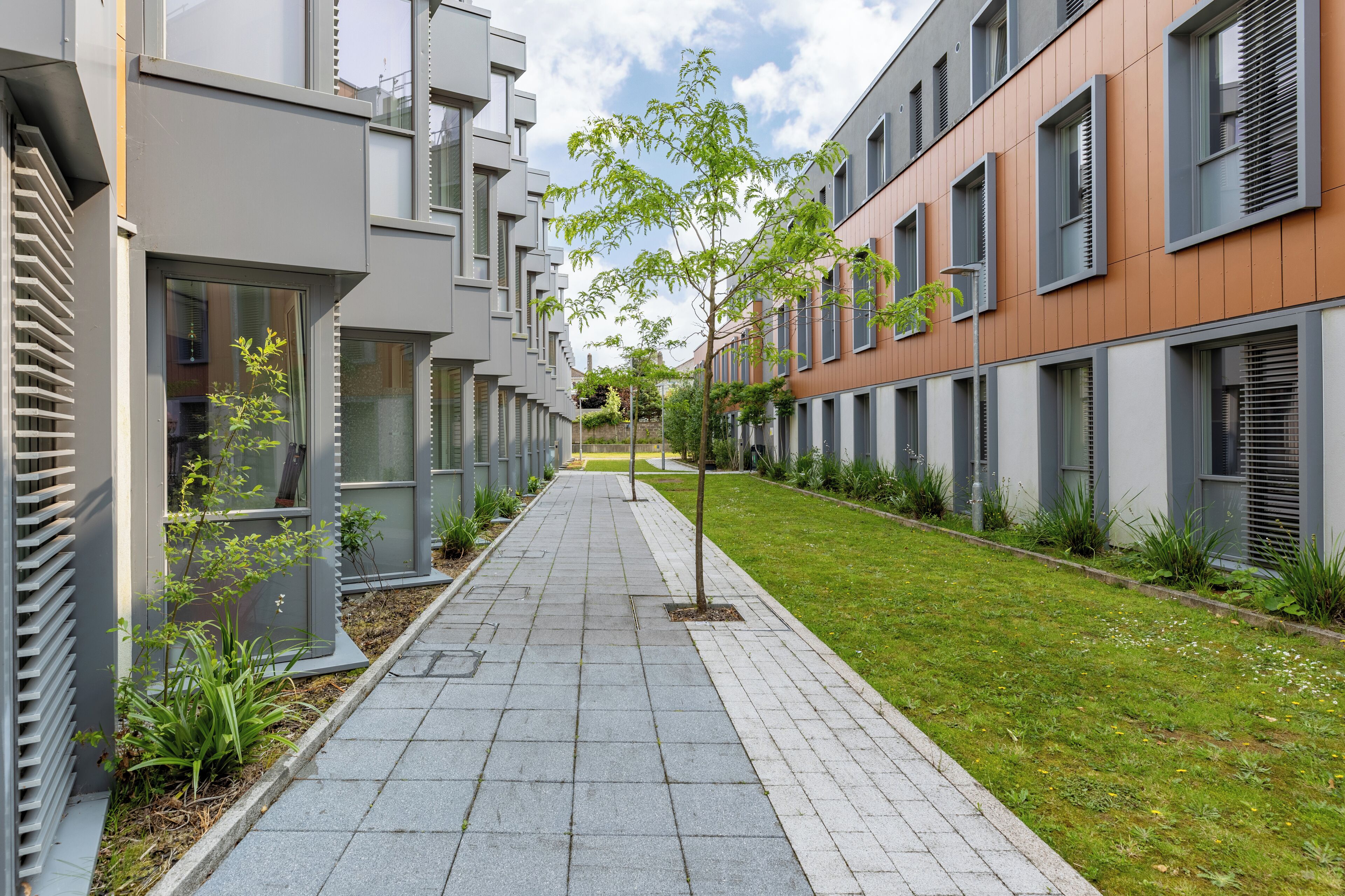 A modern apartment building with a central courtyard, featuring a paved walkway and green landscaping.