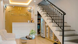 A reception area with a wooden wall, a reception desk, a staircase, and a white sofa. - Tom's Homestay Hue (Hue)