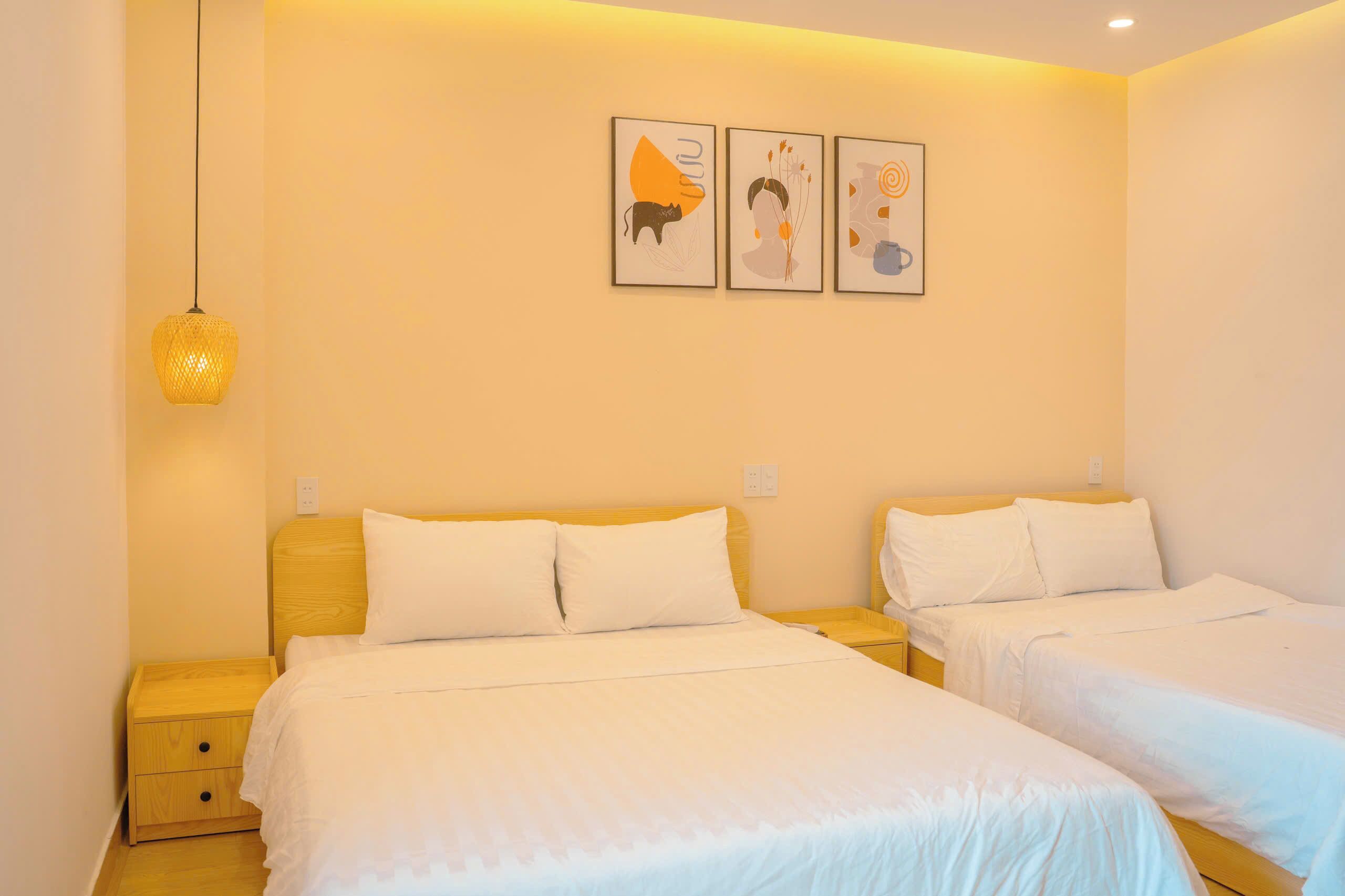 A hotel room with two beds, a hanging light fixture, and three wall-mounted artworks.