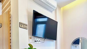 A hotel room with a flat-screen TV mounted on the wall, a potted plant, a small wooden stool, and a mirror above the counter. - Tom's Homestay Hue (Hue)
