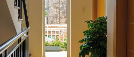 A hallway with a wooden floor, a potted plant, and a door with a number plate.