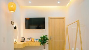 A modern room with a wooden door, a mounted TV, a wooden counter with a kettle and snacks, a small plant, and a wooden swing chair. - Tom's Homestay Hue (Hue)