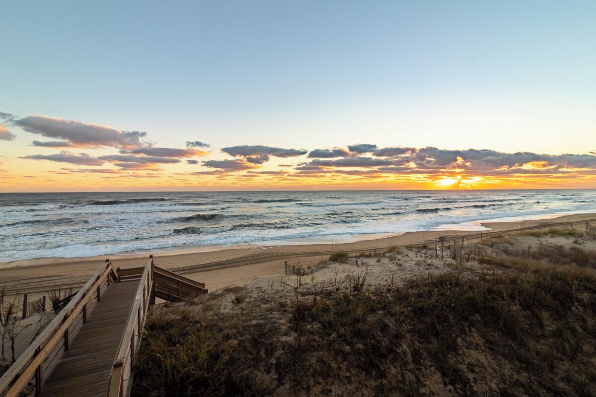 Une promenade en bois menant à une plage, avec un coucher de soleil en arrière-plan.