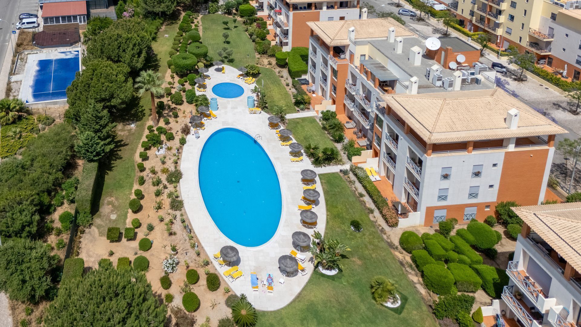 Vista aérea de una zona residencial con una gran piscina rodeada de céspedes y árboles cuidados.