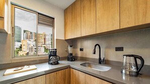 A modern kitchen with wooden cabinets, a large window, a coffee maker, a blender, a kettle, and a sink.