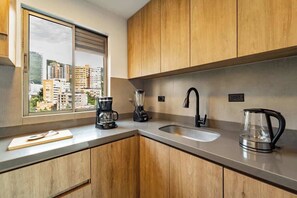 Een moderne keuken met houten kastjes, een groot raam, een koffiezetapparaat, een blender, een waterkoker en een spoelbak.
