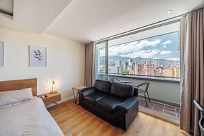 Ein modernes Hotelzimmer mit großem Fenster, einer schwarzen Ledersofa, Holzboden und einem Bett mit weißer Bettwäsche.