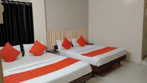 A hotel room with two beds, each with white bedding and orange accents, and a headboard with vertical lines. - Hotel Nawanagar Residency (Jamnagar)