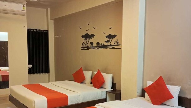 A hotel room with two beds, each with white bedding and orange accents, a mural of wildlife on the wall, and a ceiling fan. - Hotel Nawanagar Residency (Jamnagar)
