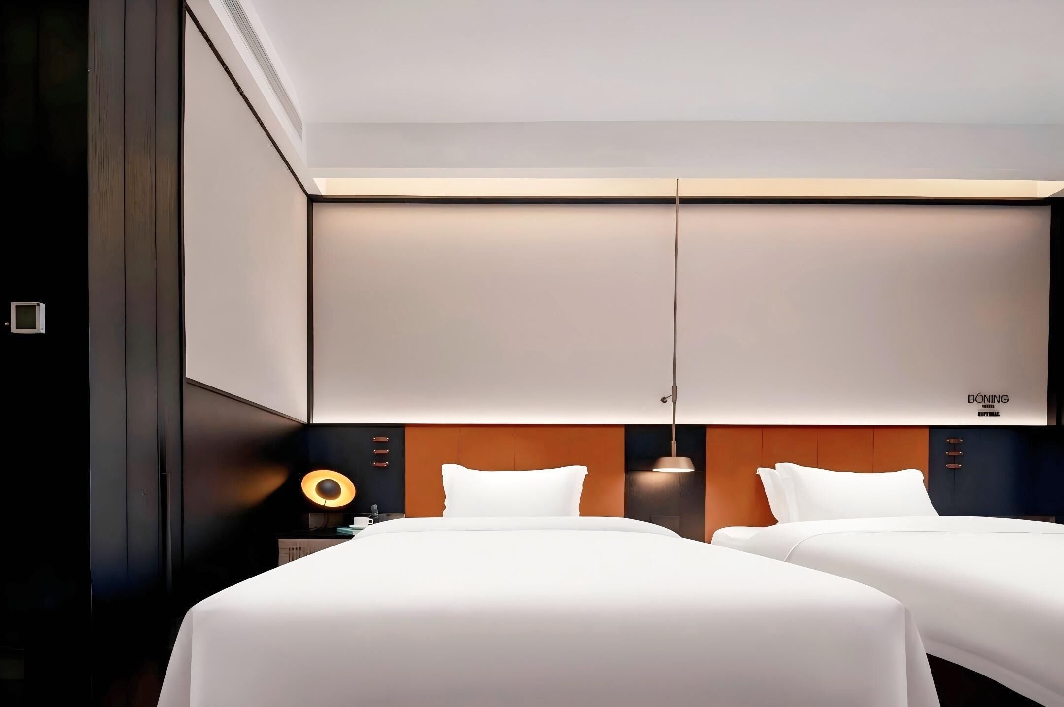 Habitación de hotel con diseño moderno, que incluye una cama grande con ropa blanca, cabecera de madera y una lámpara colgante.