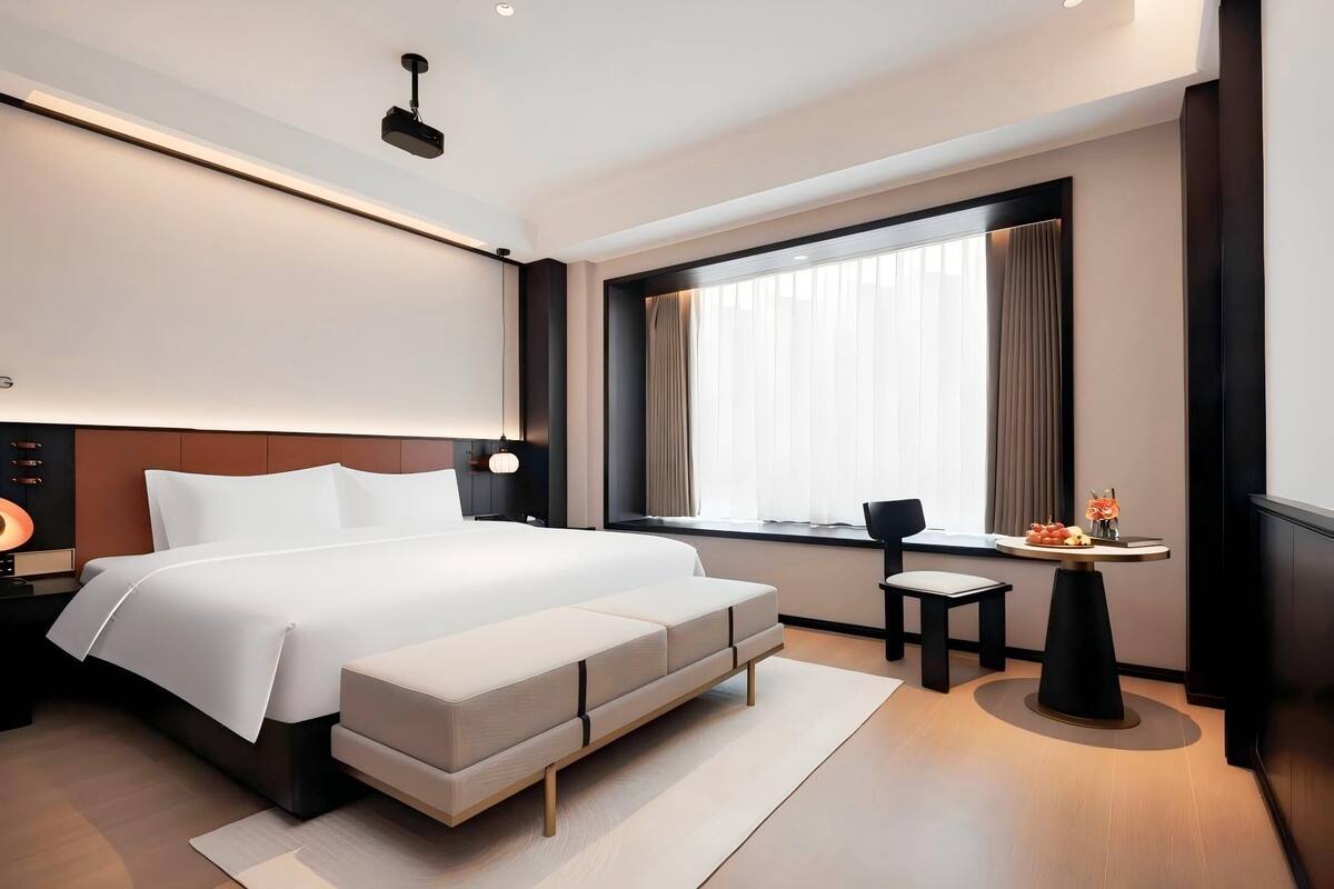 A modern hotel room with a large bed, bedside tables, a desk, and a window with curtains.