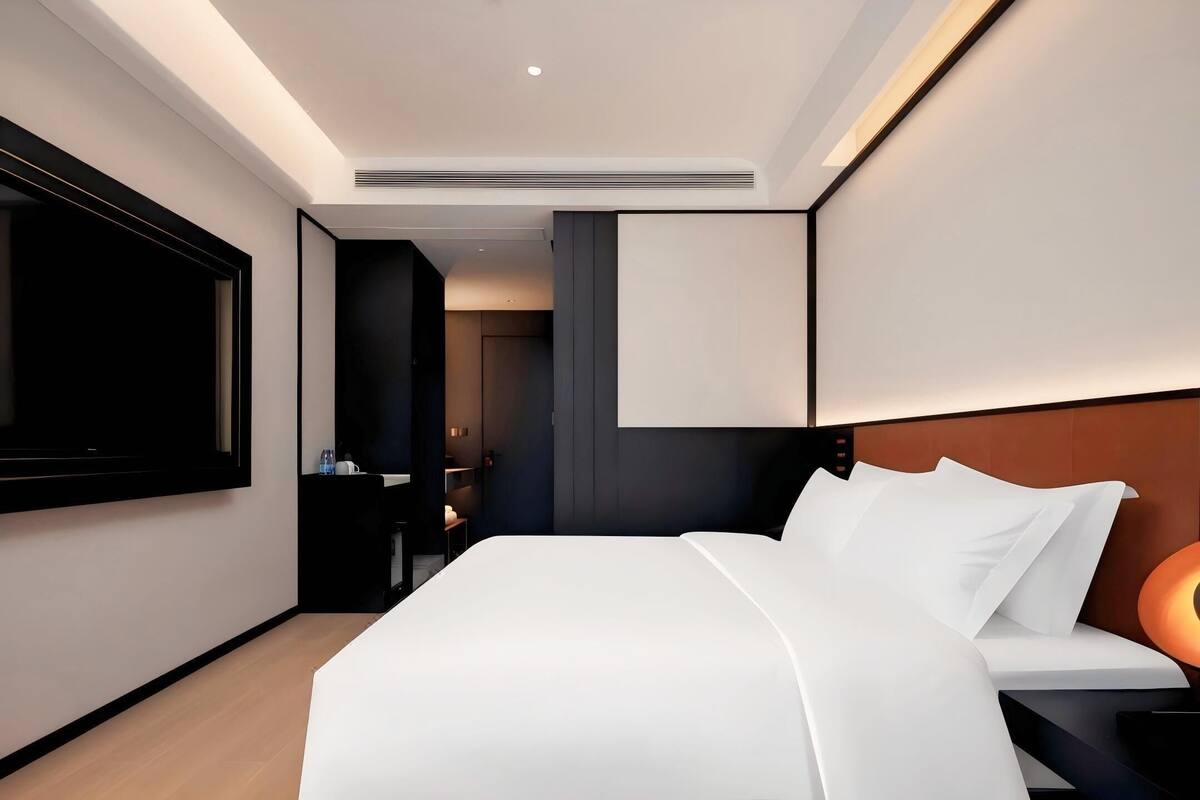 A modern hotel room with a large bed, a flat-screen TV, and a bedside table with a lamp.