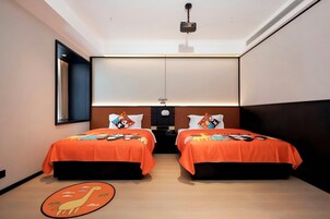 Habitación de hotel con dos camas, cada una con cubrecama naranja y almohadas a juego, un proyector montado en el techo y suelo de madera.