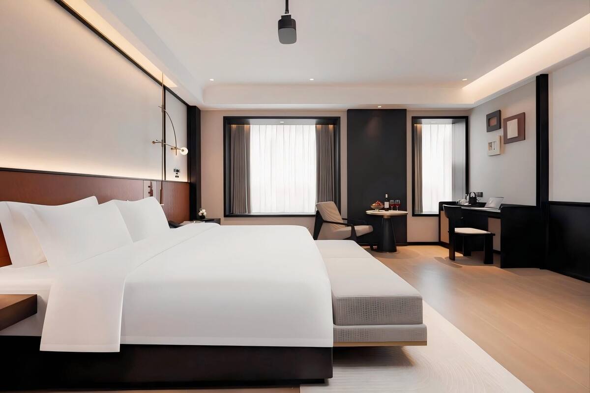 A modern hotel room with a large bed, a desk with a laptop, and a chair.
