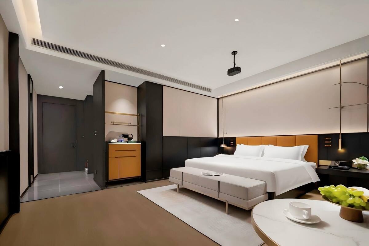 A modern hotel room with a large bed, bedside tables, a desk, and a seating area.