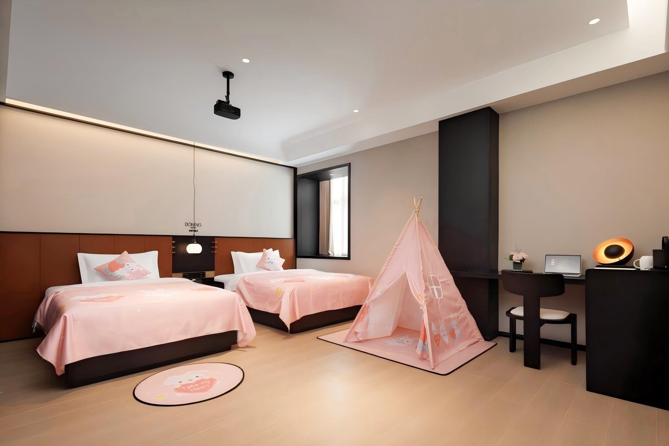 A modern hotel room with two beds, a desk, a chair, a laptop, and a small tent-like structure.