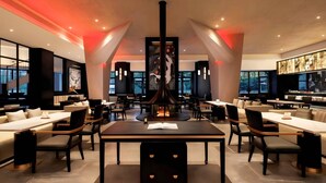 A modern restaurant with a central fire feature, multiple dining tables, and contemporary decor. - BONINGHOTEL (Meishan)