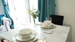 A dining table set with white plates, bowls, and a glass, accompanied by a vase with green foliage.