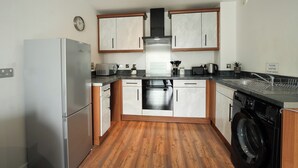 A modern kitchen with white cabinets, a stainless steel refrigerator, a built-in oven, a washing machine, and a sink.