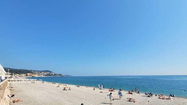 Una playa con gente tomando el sol y nadando.