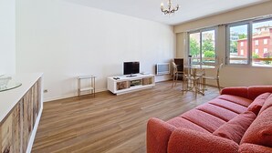 Una sala moderna con piso de madera, un sofá rojo, un televisor y un comedor con sillas y una mesa.