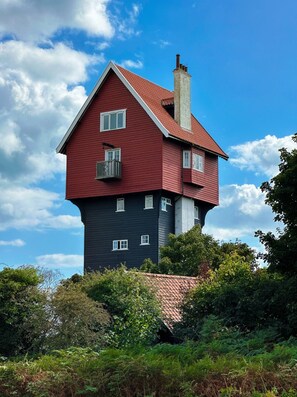 A two-story house with a red roof and a chimney, surrounded by greenery.