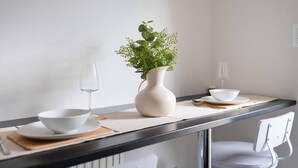 Eine moderne Küche mit weißer Arbeitsplatte, einer weißen Vase mit Grünpflanzen und weißem Geschirr.