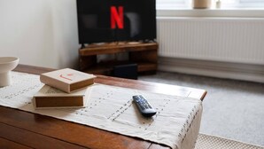 Ein gemütliches Wohnzimmer mit Couchtisch aus Holz, einer Fernbedienung und Büchern. Ein Fernseher mit Netflix-Logo ist an der Wand befestigt.