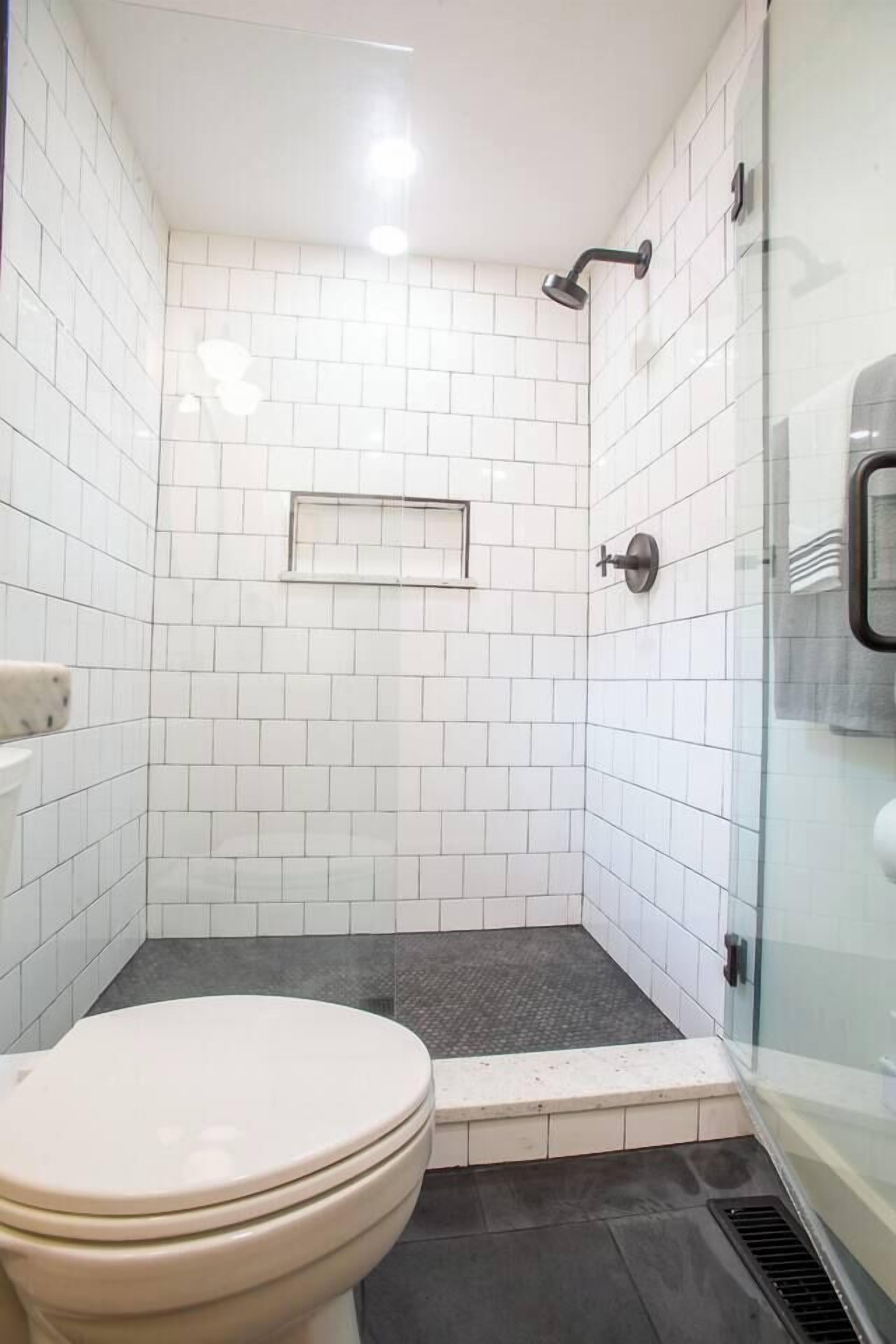 Un baño pequeño y moderno con azulejos blancos, cabina de ducha de vidrio y un inodoro.