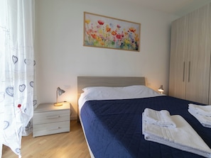 Een slaapkamer met een bed, nachtkastje, lade, schilderij en een kledingkast.