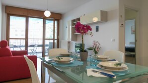 A modern dining area with a glass table set for four, surrounded by white chairs. - Sweet Home Daniele – appartamento in centro e ... (Lecco)