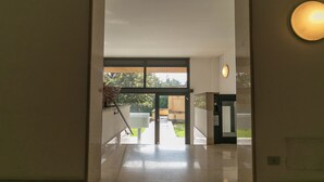 A hallway with a glass door leading outside, a wheelchair-accessible elevator, and a planter with plants. - Sweet Home Daniele – appartamento in centro e ... (Lecco)