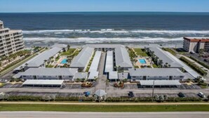 A coastal hotel with multiple buildings, a parking lot, and a view of the ocean.