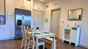 Una cocina moderna con armarios de madera, un refrigerador de acero inoxidable, una mesa de comedor con sillas y un pequeño armario blanco con espejo.
