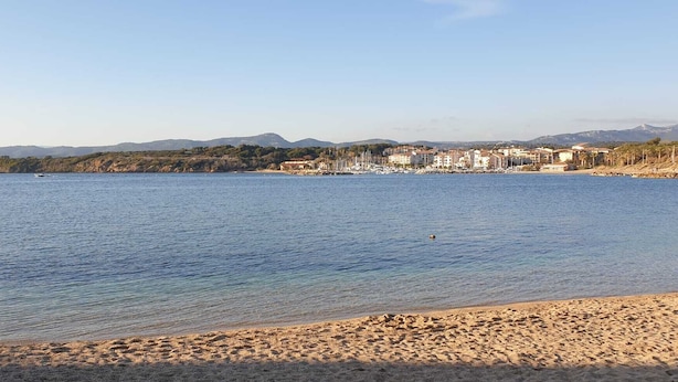 Una playa con agua cristalina, una orilla arenosa y un pueblo al fondo.