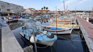 Un puerto deportivo con varias embarcaciones amarradas, un edificio con tiendas y un cielo despejado.